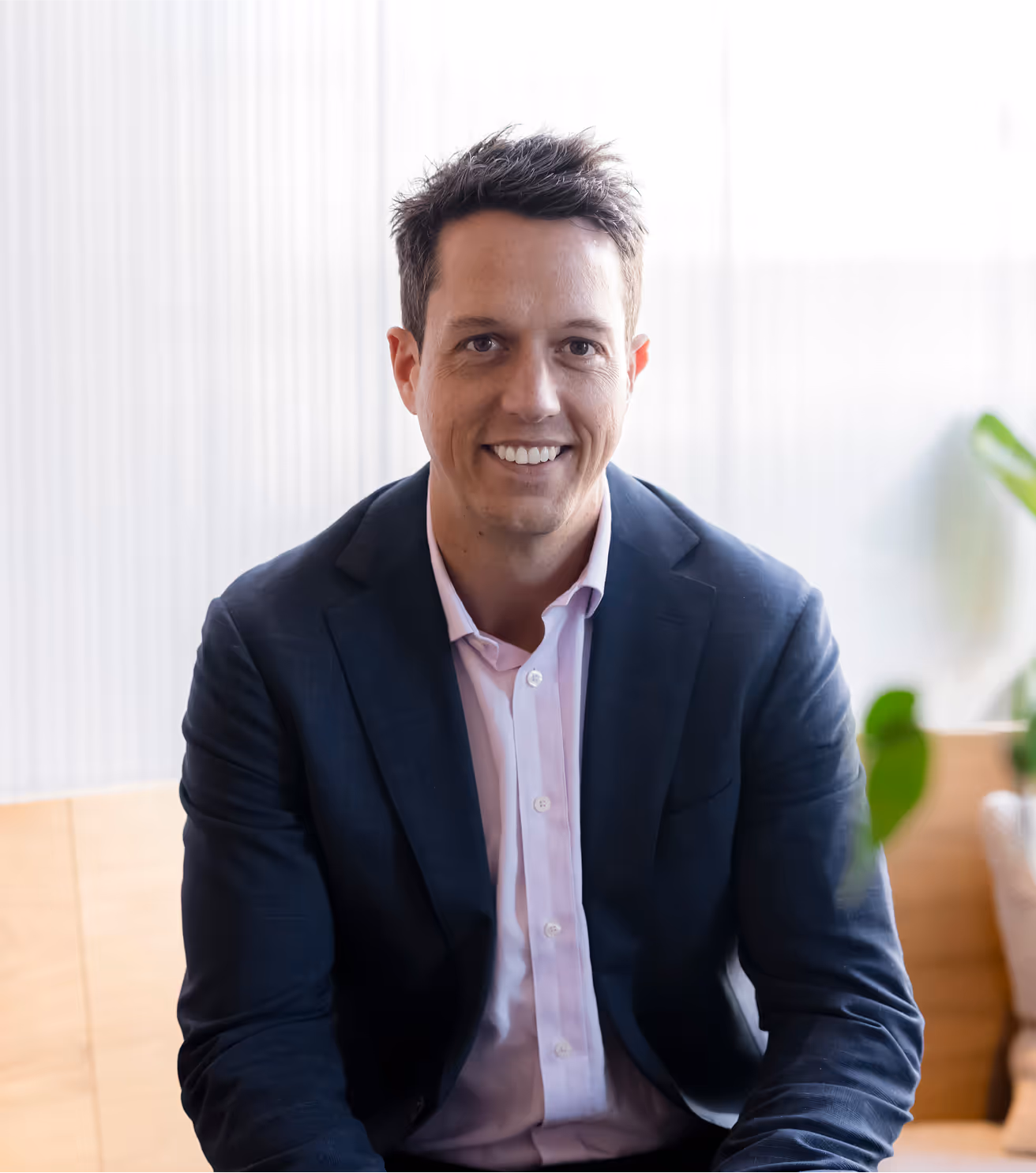 Man in suit and pink shirt smiles at the camera