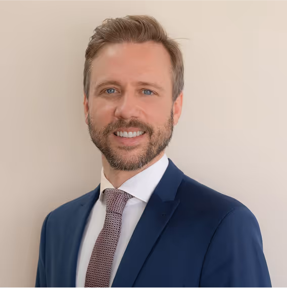 Man in suit and tie smiles against a neutral background