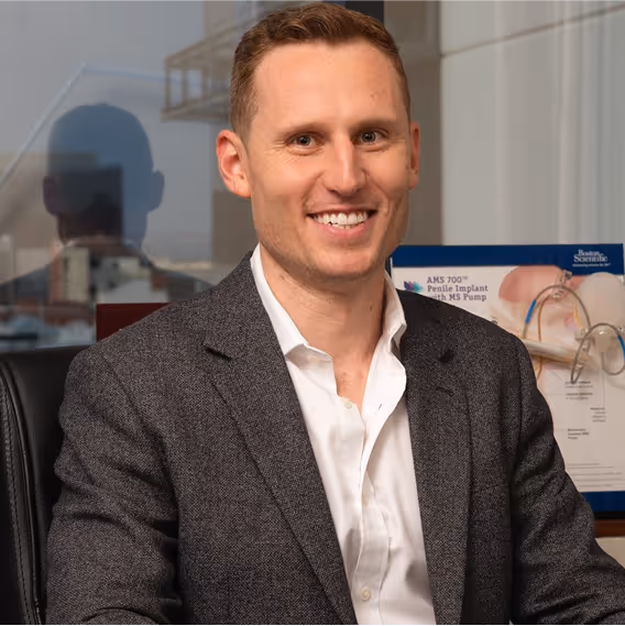 Smiling man in gray blazer sits in front of Boston Scientific product
