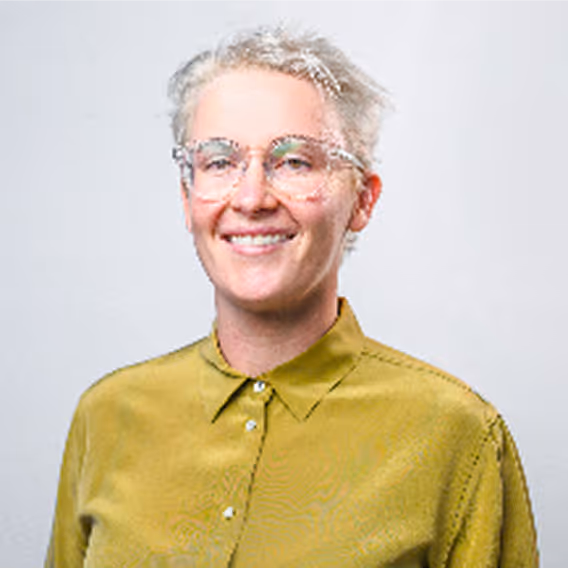 Person with short white hair, glasses, and a yellow shirt smiles