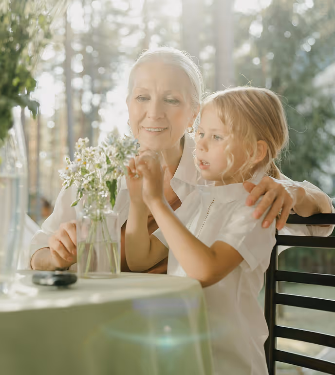 Grandmother and granddaughter sit at a table with flowers outside
