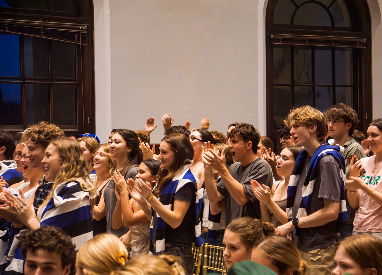A group of young people standing indoors, clapping and cheering enthusiastically.