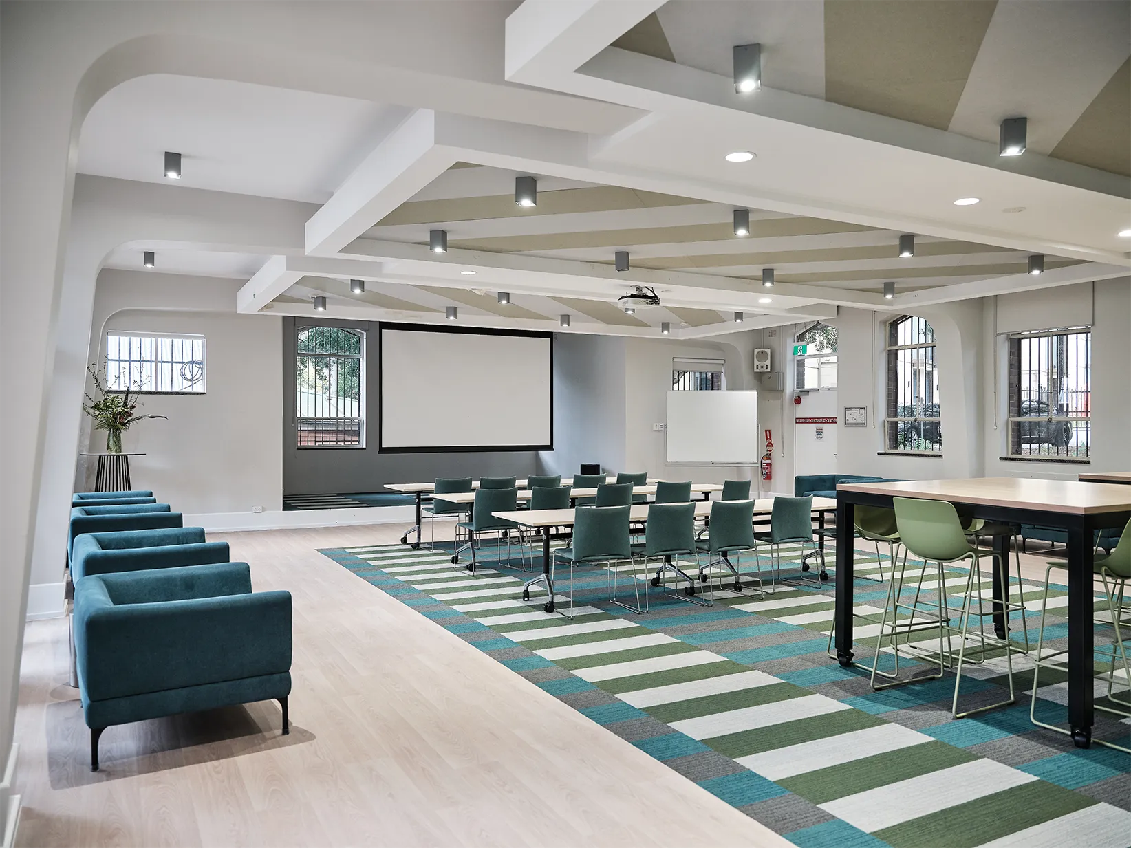 Modern classroom with green chairs, blue armchairs, large projector screen, and striped carpet.