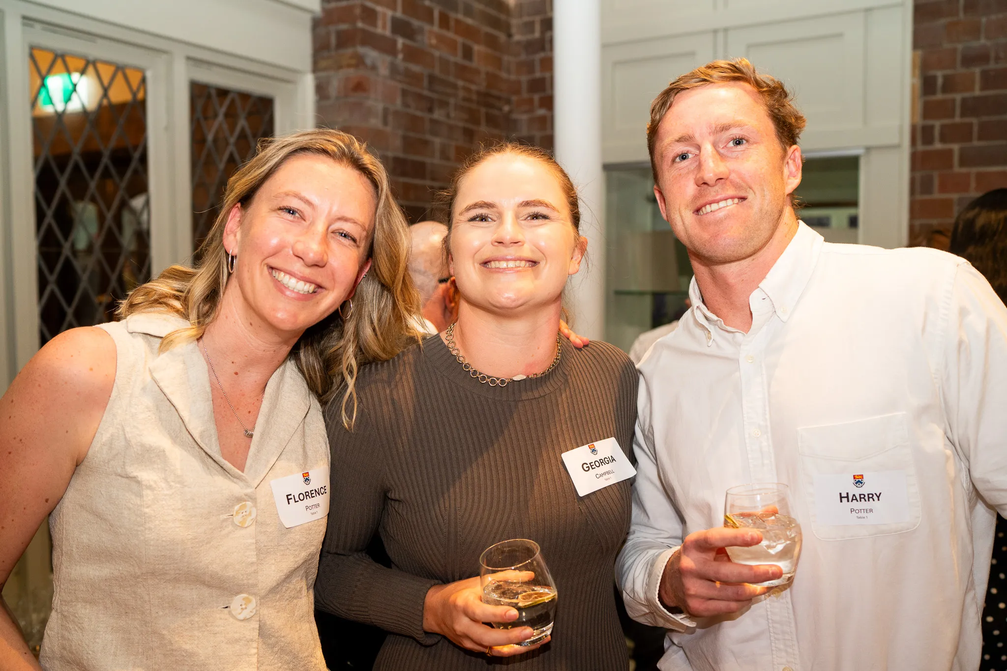 Three people smiling and holding drinks at a social event indoors.