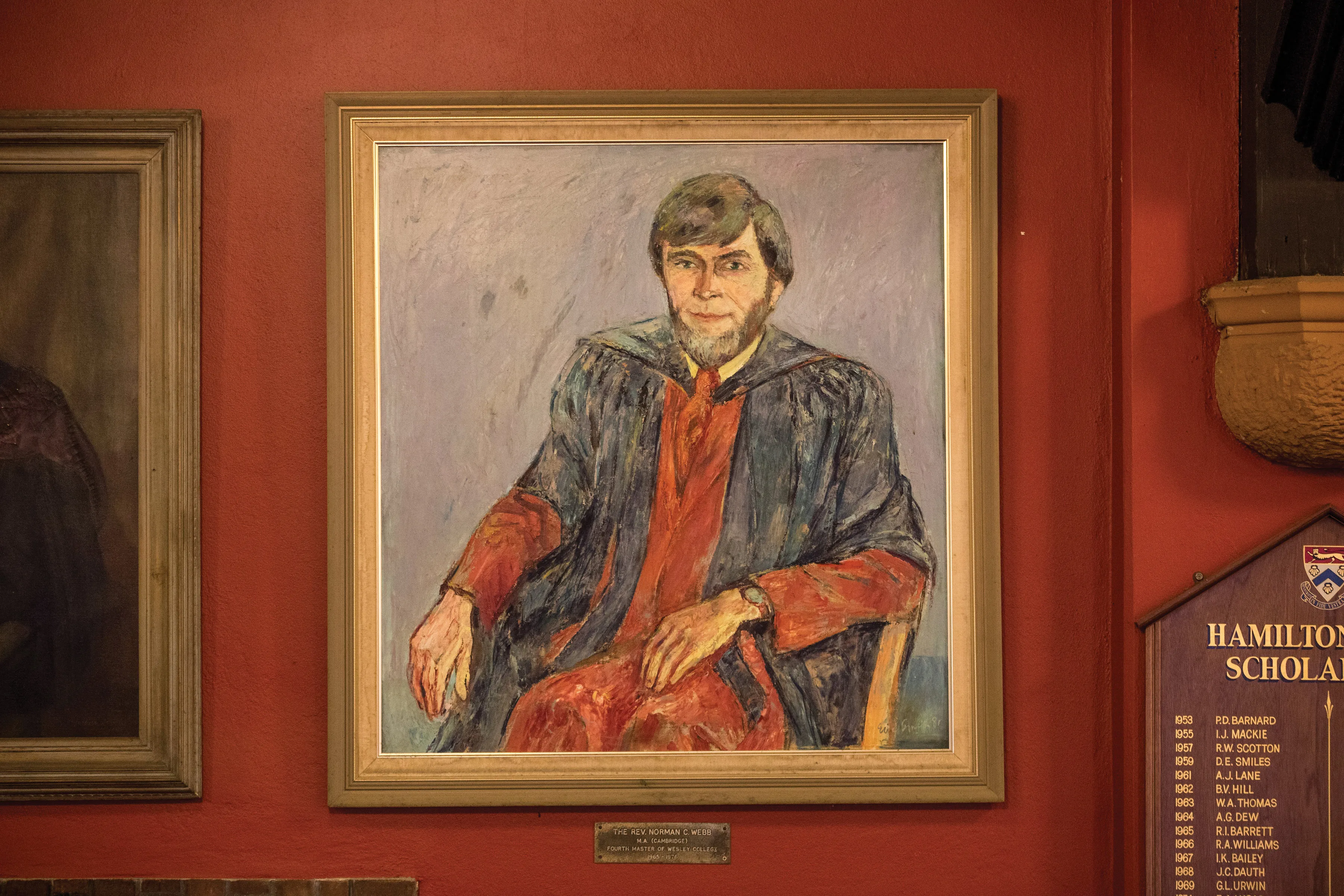 Framed painting of a man with a beard wearing academic robes, seated on a chair against a red wall.