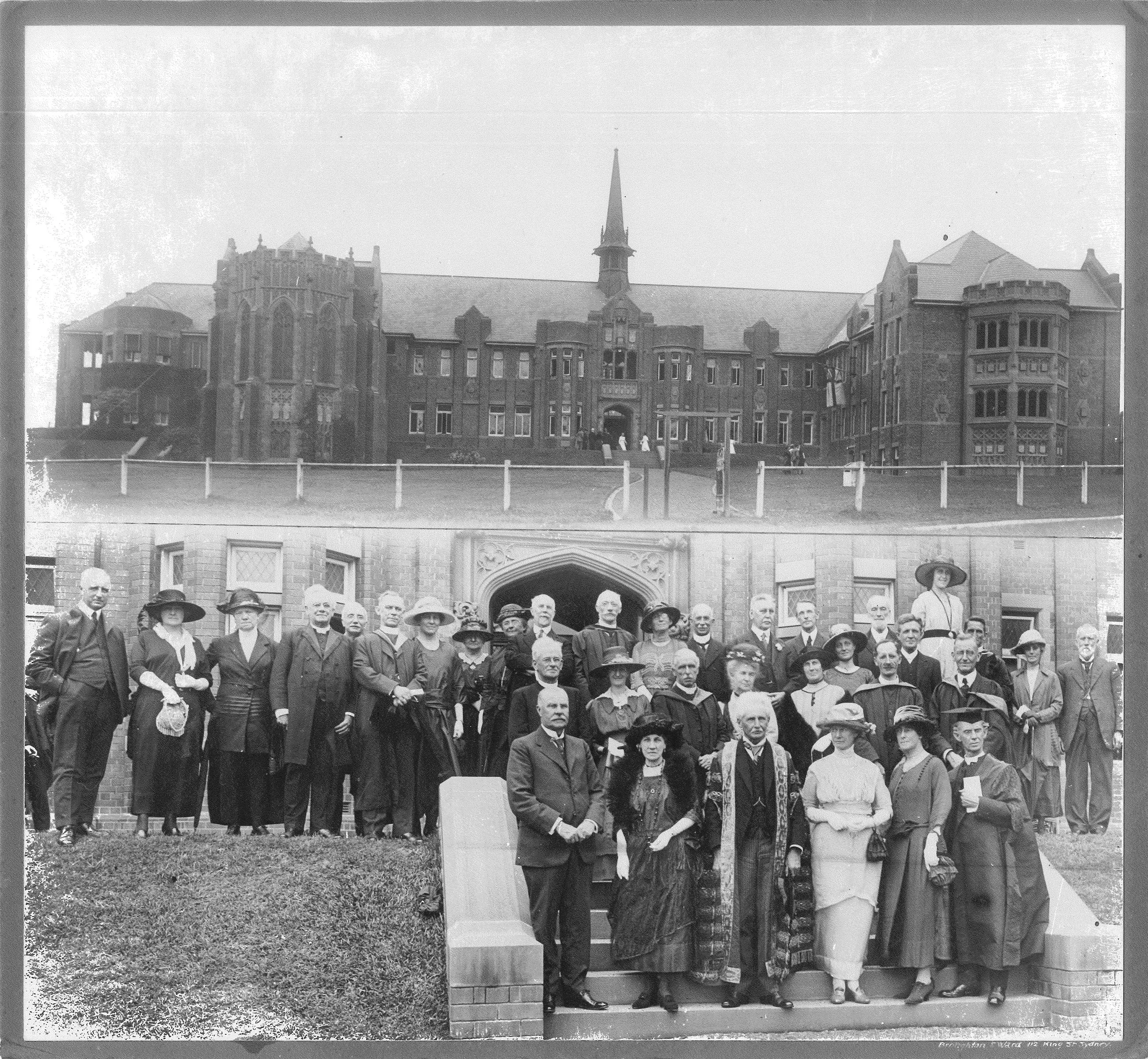 Black and white historical photograph of a large group of formally dressed men and women standing on steps and in front of a large brick building with a central spire.