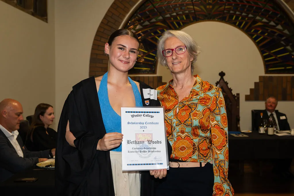 Two women smiling at a scholarship award ceremony, one holding a certificate from Wesley College.