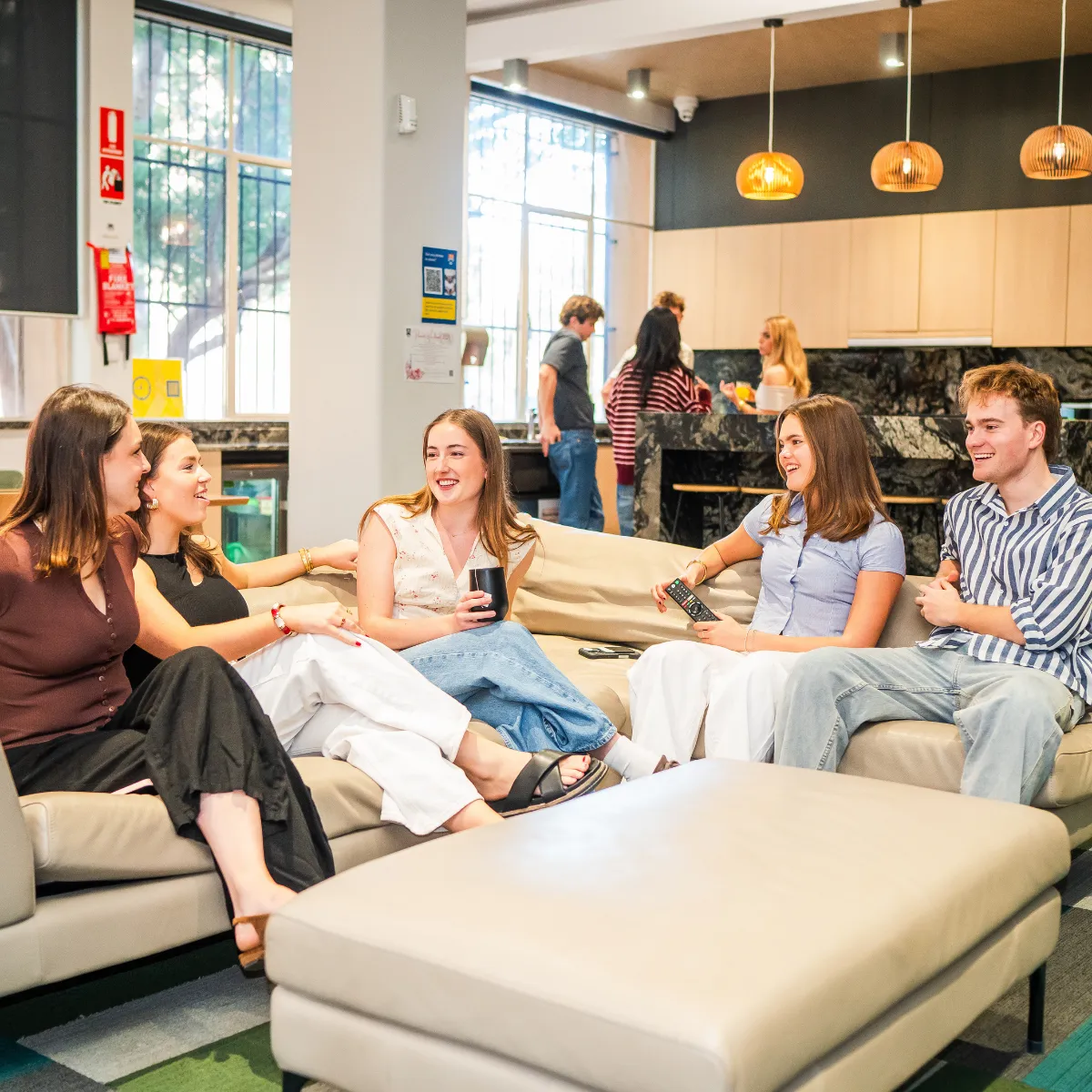 Group of young adults sitting on couches in a modern common area, socializing and smiling.