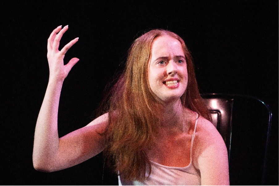 The image shows a person with long, wavy hair, wearing a white sleeveless top, raising their right hand with their palm facing outward.AI-generated content may be incorrect.