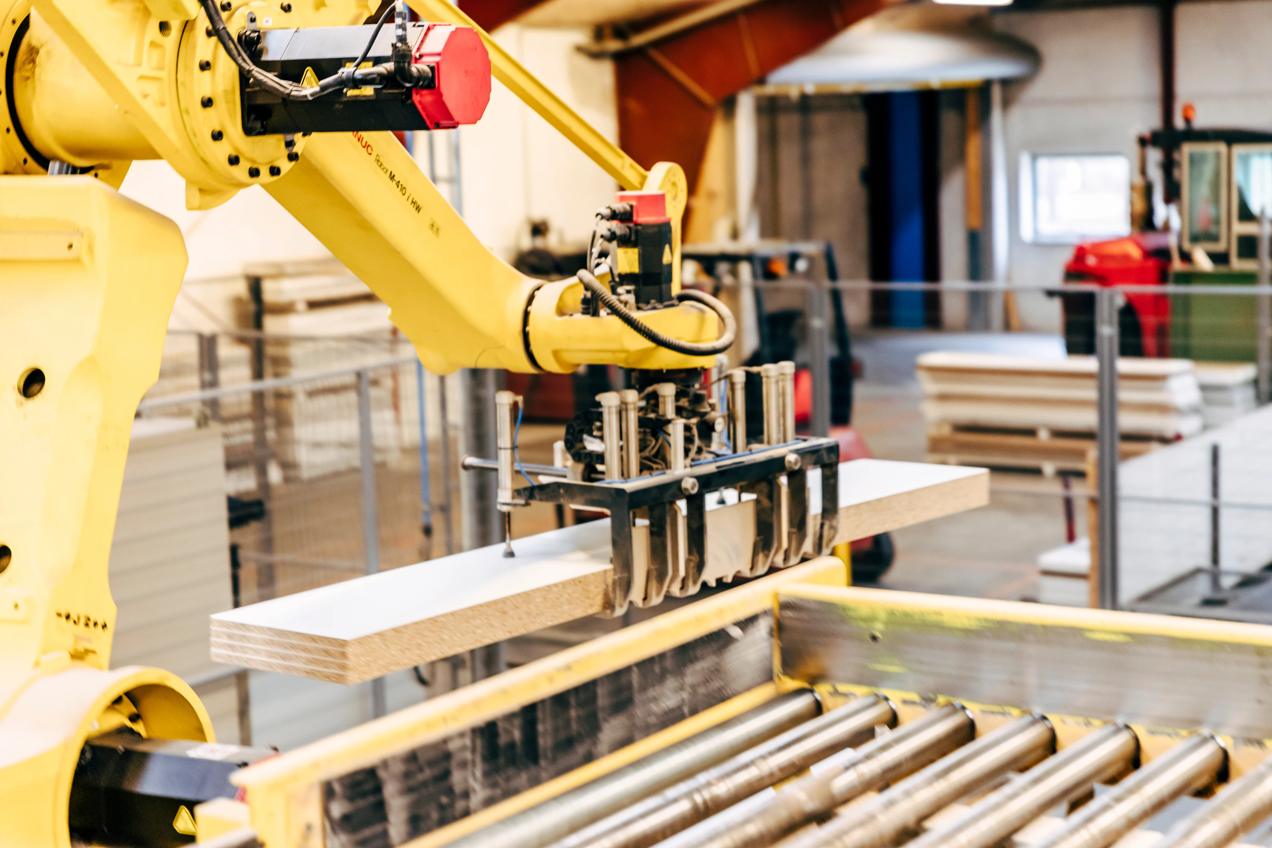 Robotarm håndterer et træplade i en produktionslinje med ruller i en fabrik.