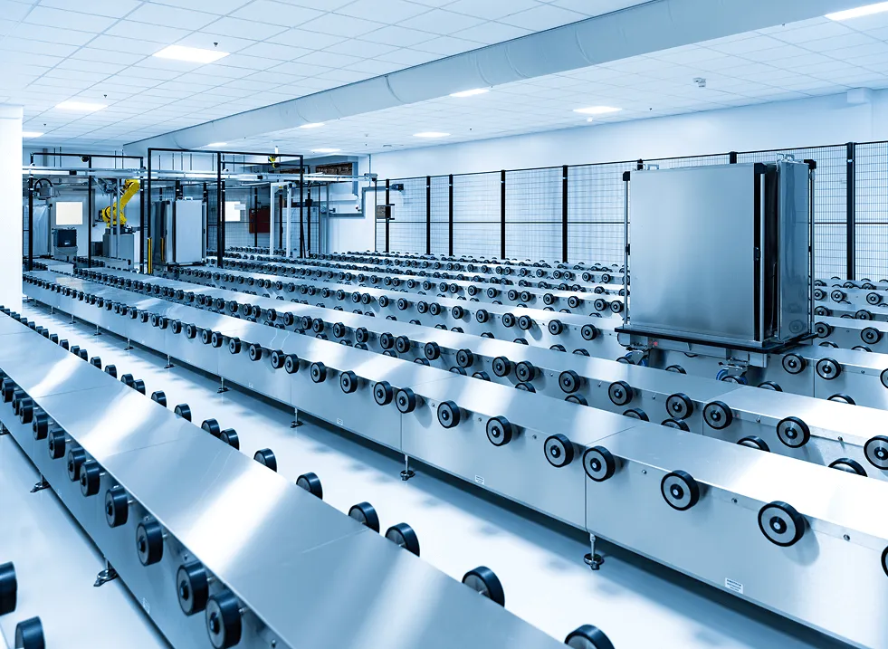 Große industrielle Produktionslinie mit Metallwalzen und Roboterarm in einem hellen Raum.