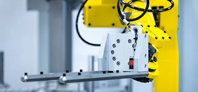 Ein gelber Industrieroboterarm mit einem Greifwerkzeug aus Metall in einer Fabrik.