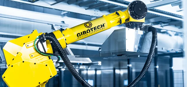 Ein gelber Industrieroboterarm der Marke Gibotech in einer Fabrikumgebung mit Metallkonstruktionen im Hintergrund.