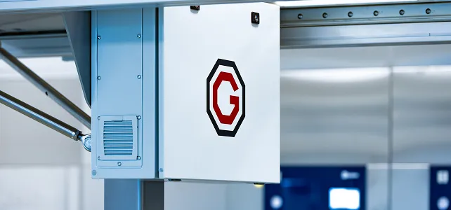 Weißes Bedienfeld mit einem roten und schwarzen G-Logo, montiert auf einem Metallständer in einer industriellen Umgebung.