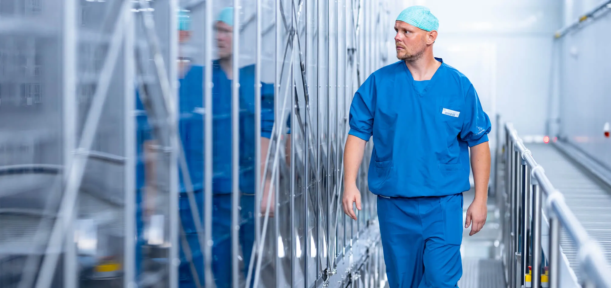 Ein Mann in blauem OP-Kittel geht durch einen sterilen, hochtechnologischen Flur in einer medizinischen Einrichtung.