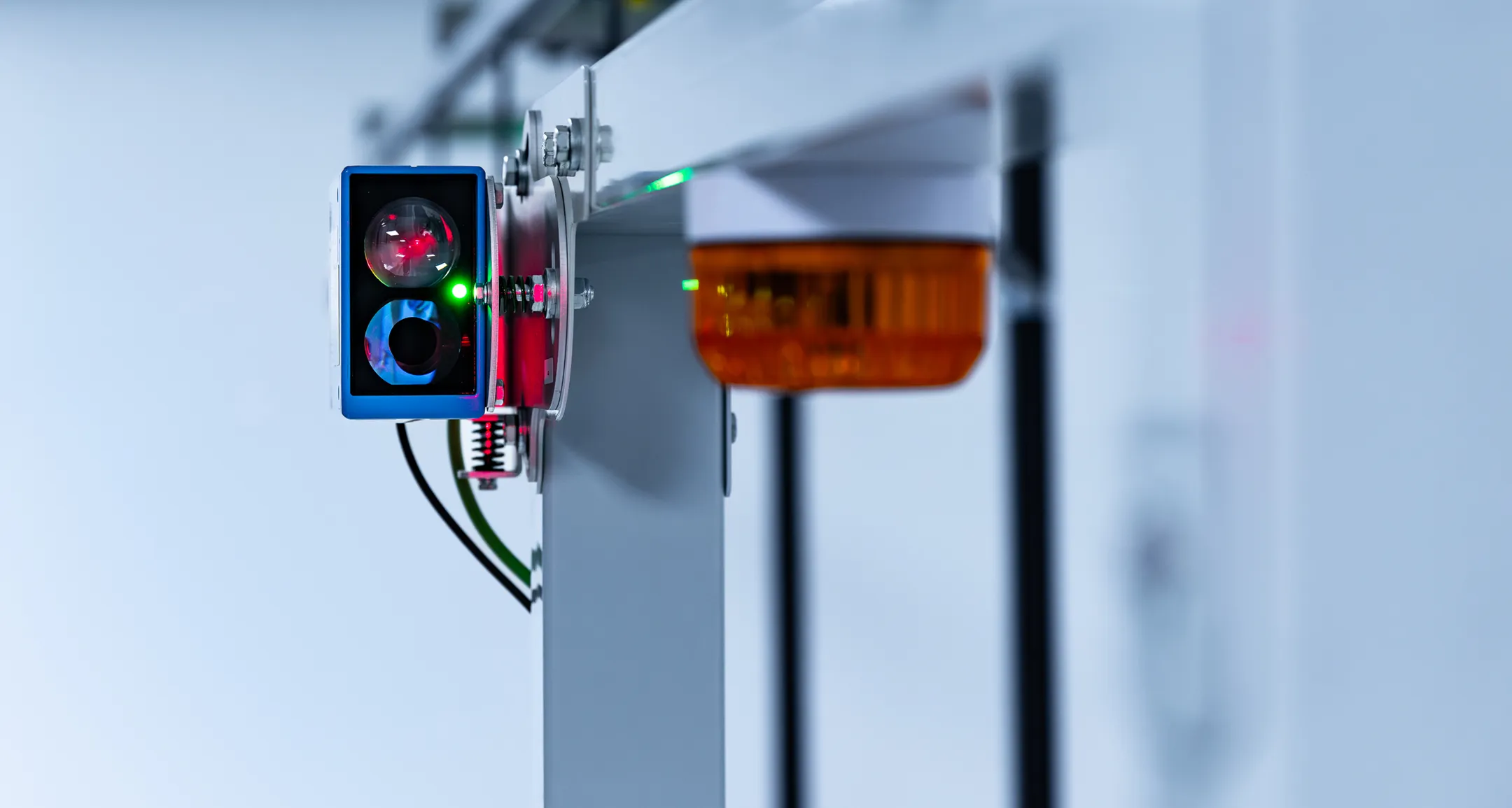 Nahaufnahme eines Sensors und eines Blinkers, montiert auf einem Metallrahmen in einer industriellen oder technologischen Umgebung.