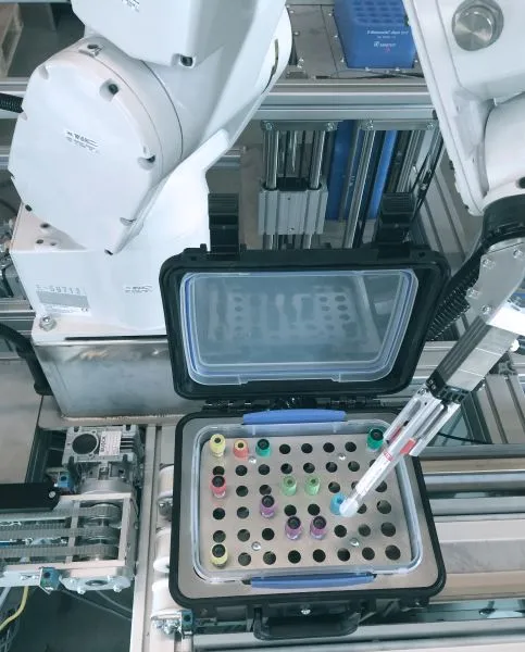 Robot arm handling test tubes in a laboratory automation system with an open container.