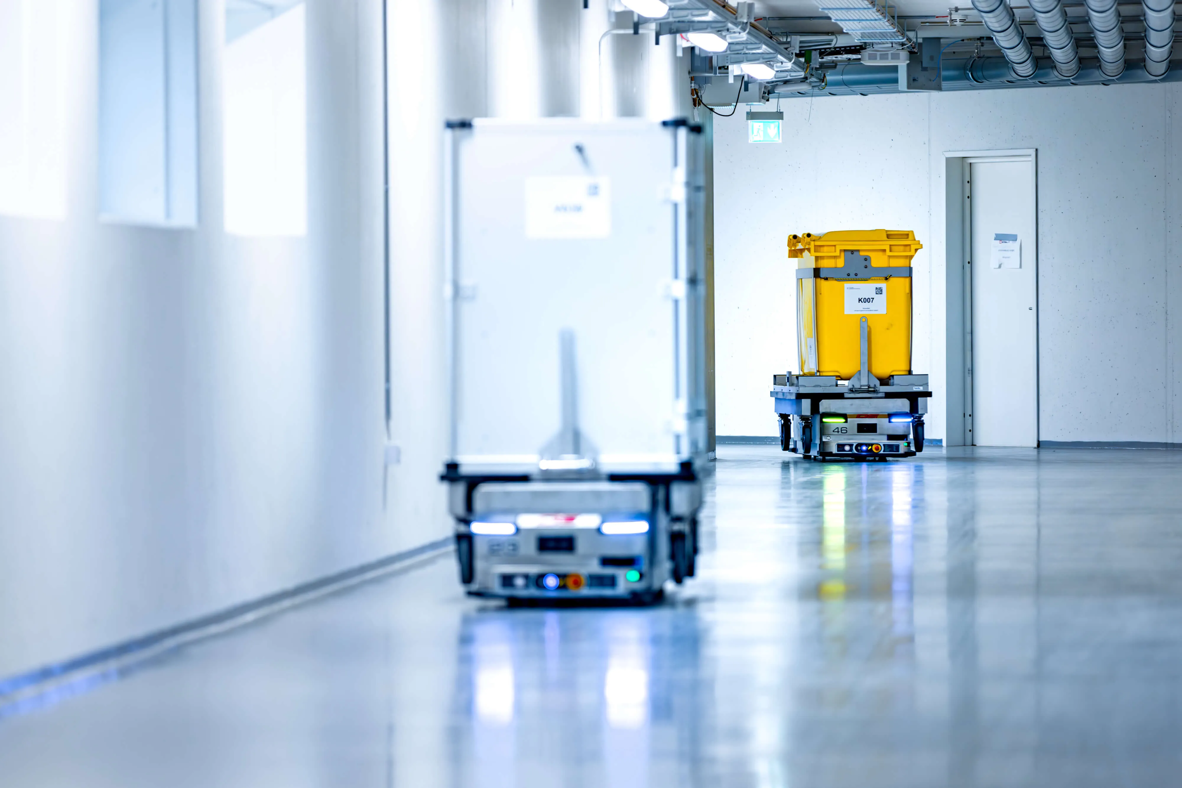 To autonome transportrobotter bevæger varer gennem en industriel gang med blankt gulv.