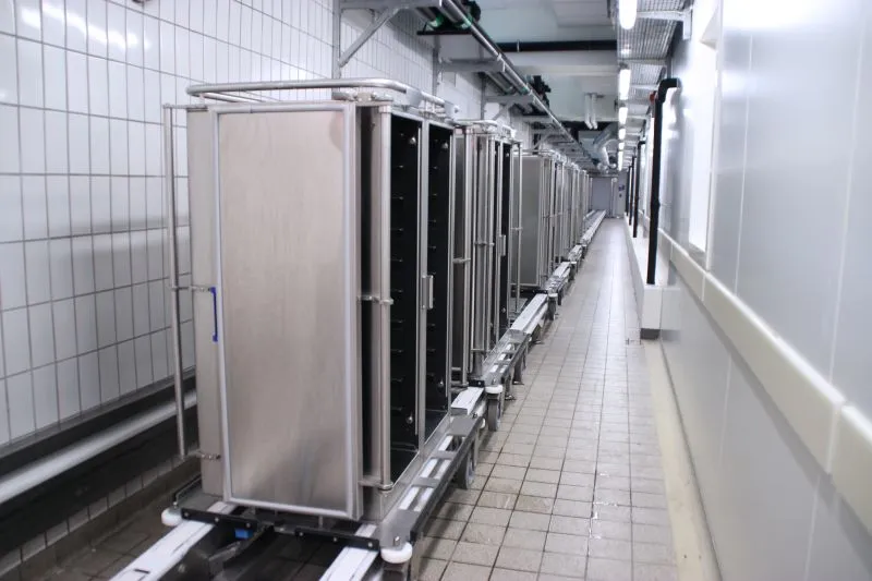 Lang række af automatiserede metalvogne på et skinnebaseret transportsystem i et køkkenmiljø.