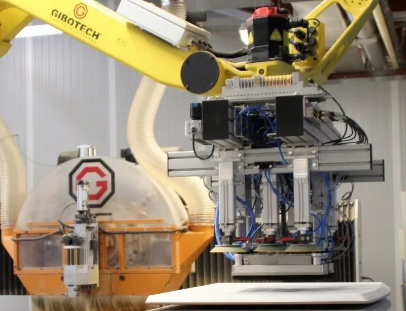 Industrielt robotarm med flere slanger og ledninger i en produktionshal.