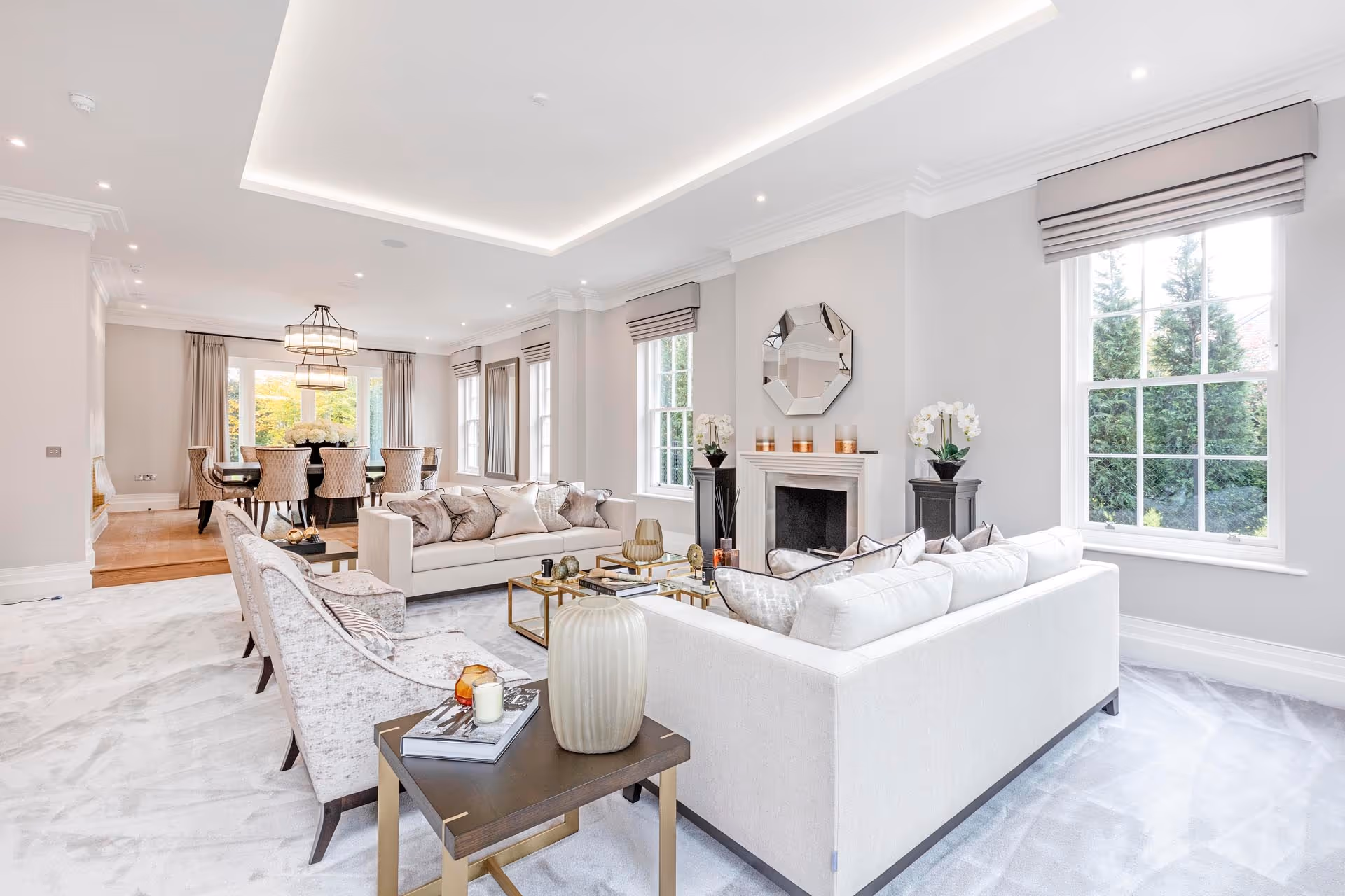 Bright living room with cream sofas, a fireplace with a mirror above and a dining area beyond