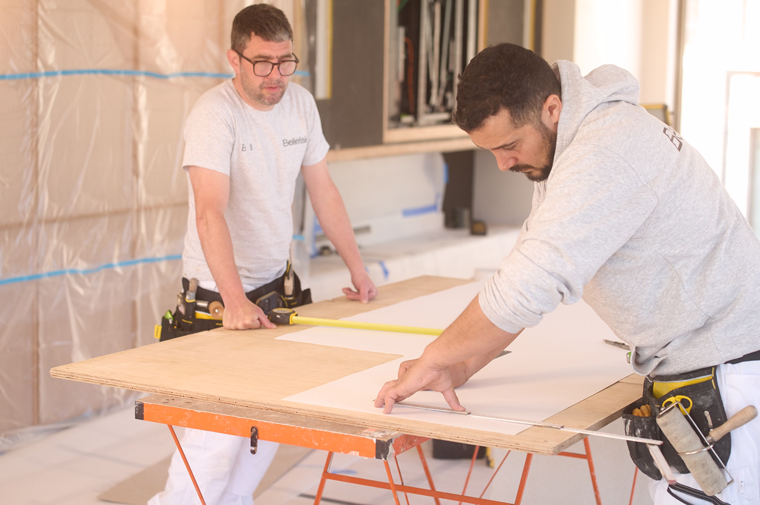 Two Bellefair decorators measuring and cutting wallpaper on a work table