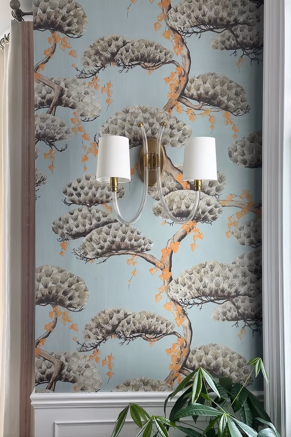 Pine tree pattern wallpaper behind a brass wall light, above white panelling