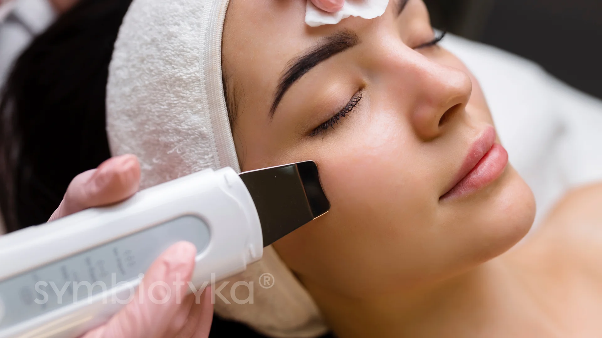 Woman receiving ultrasonic facial treatment with a skin scrubber on her cheek.
