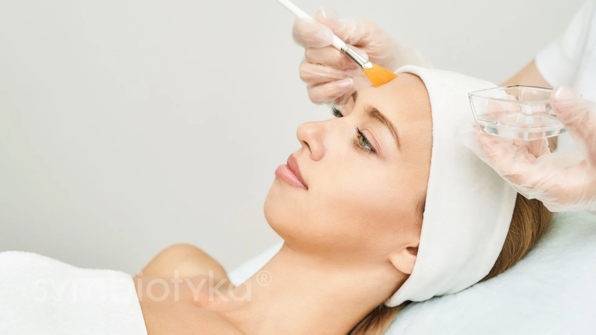 Woman receiving a facial treatment with a brush applying skincare product on her forehead.