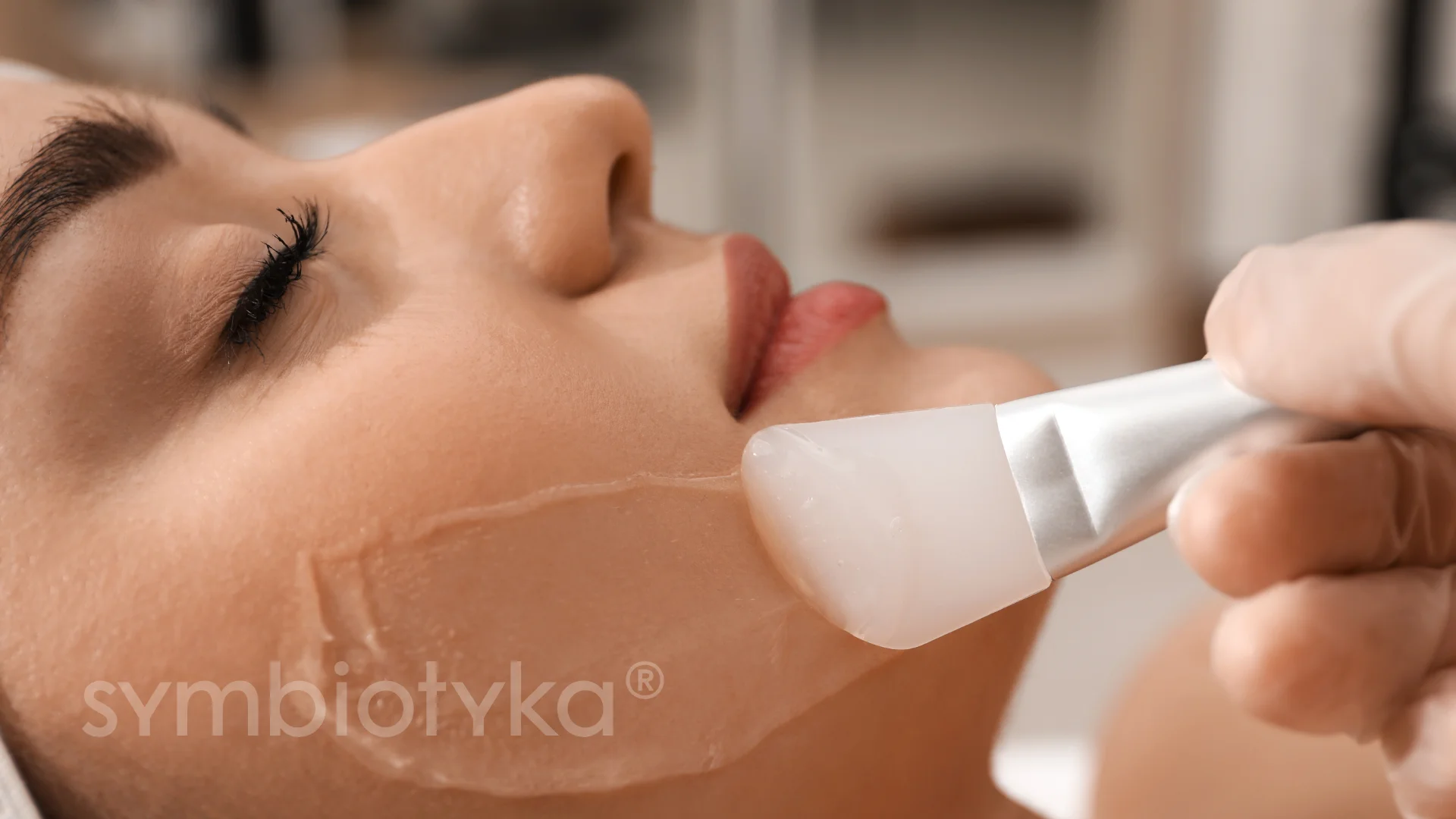 Close-up of a facial treatment being applied on a woman's cheek with a silicone spatula.