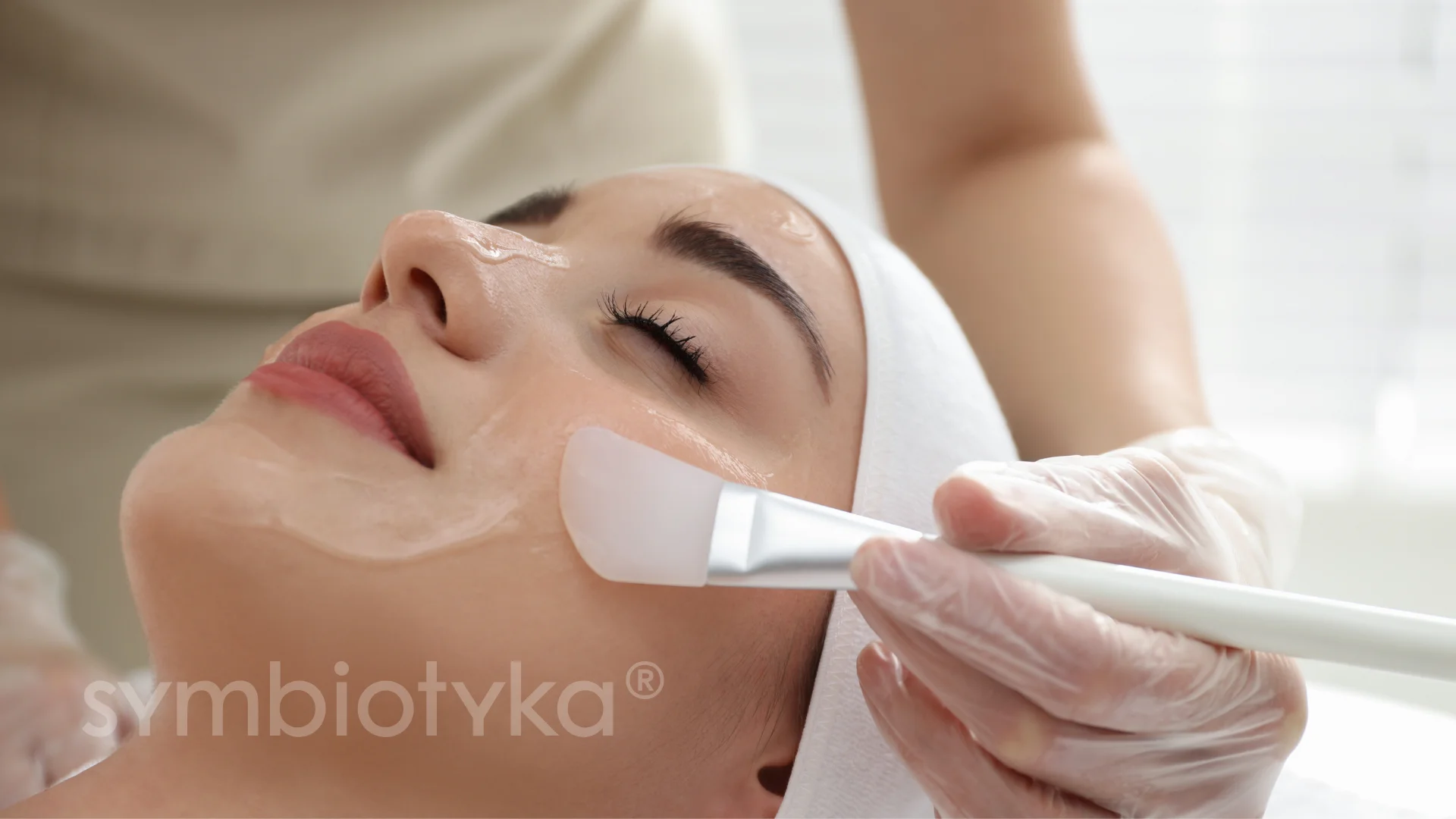 Woman with eyes closed receiving facial treatment with a brush applying a skincare product.