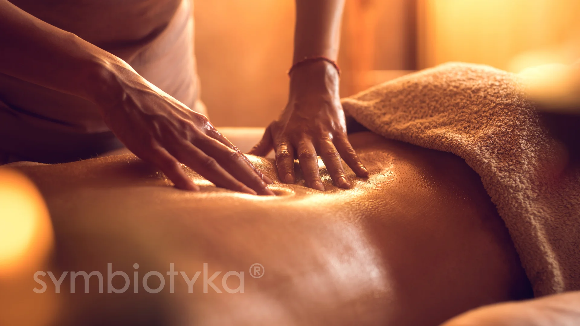 Hands giving a relaxing oil massage on a person's back with a towel covering part of the body.