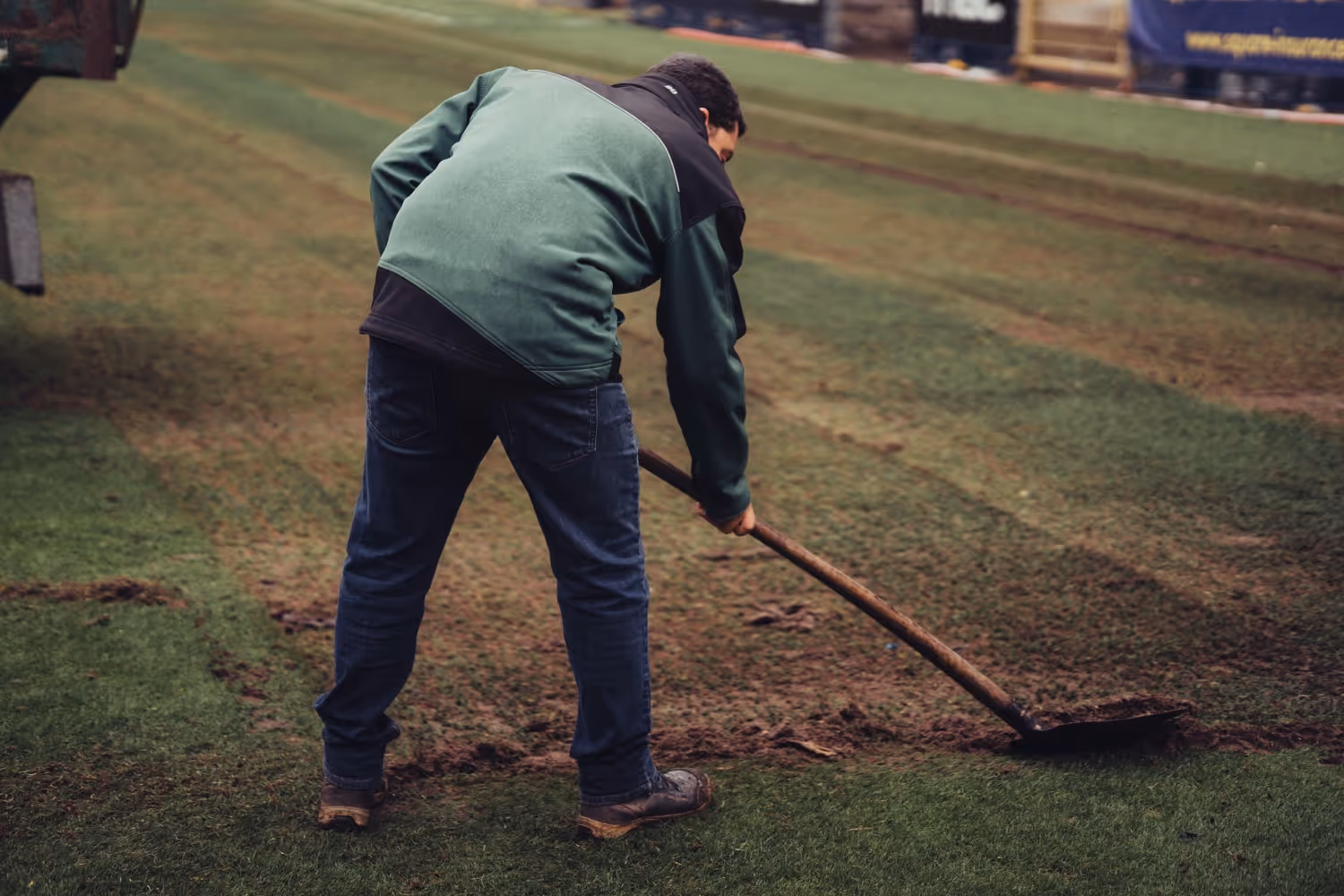 Man aan het schoffelen van een grasveld met een lange schop.