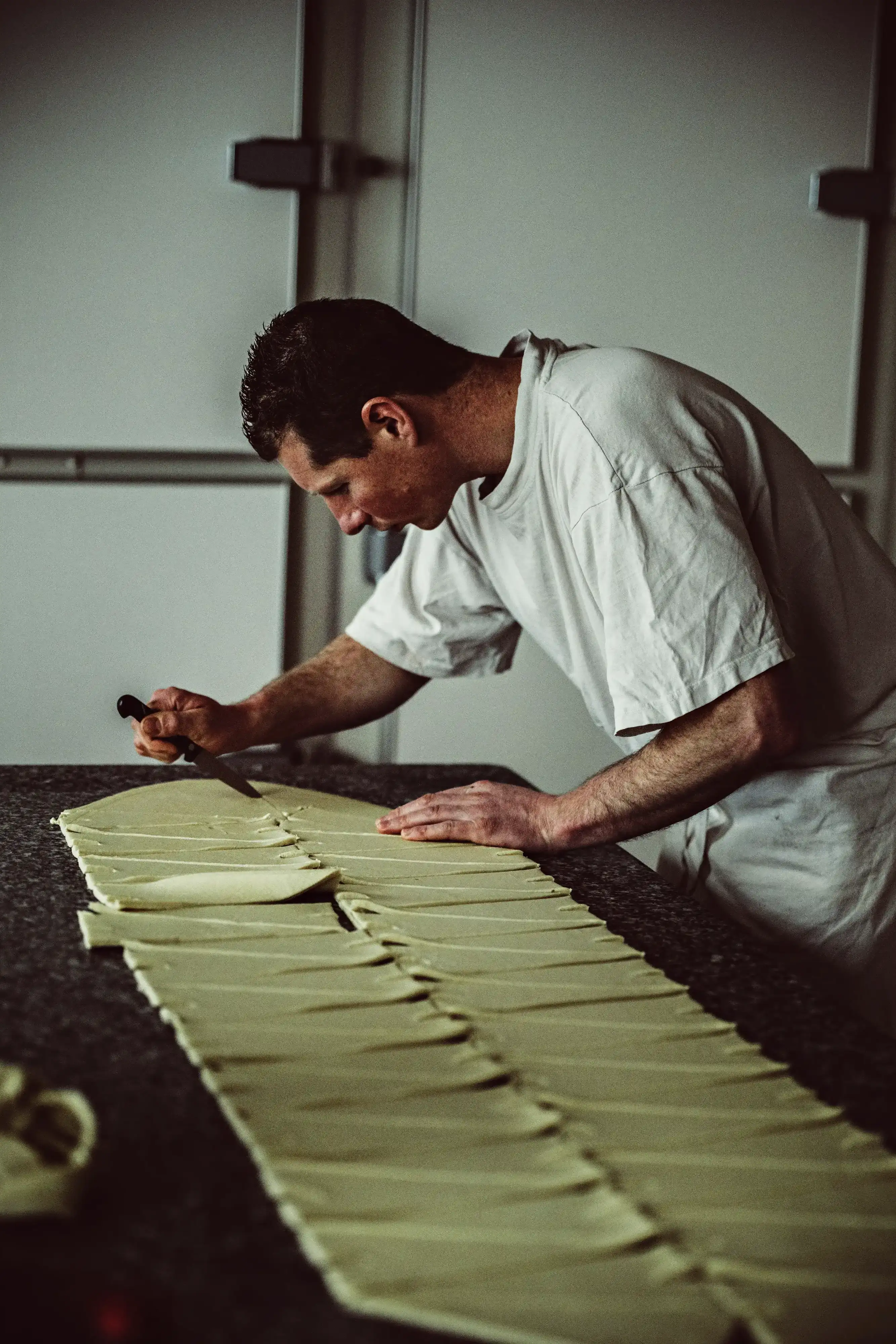 An artisan baker cuts puff pastry into regular triangles, a preparatory step before making croissants.