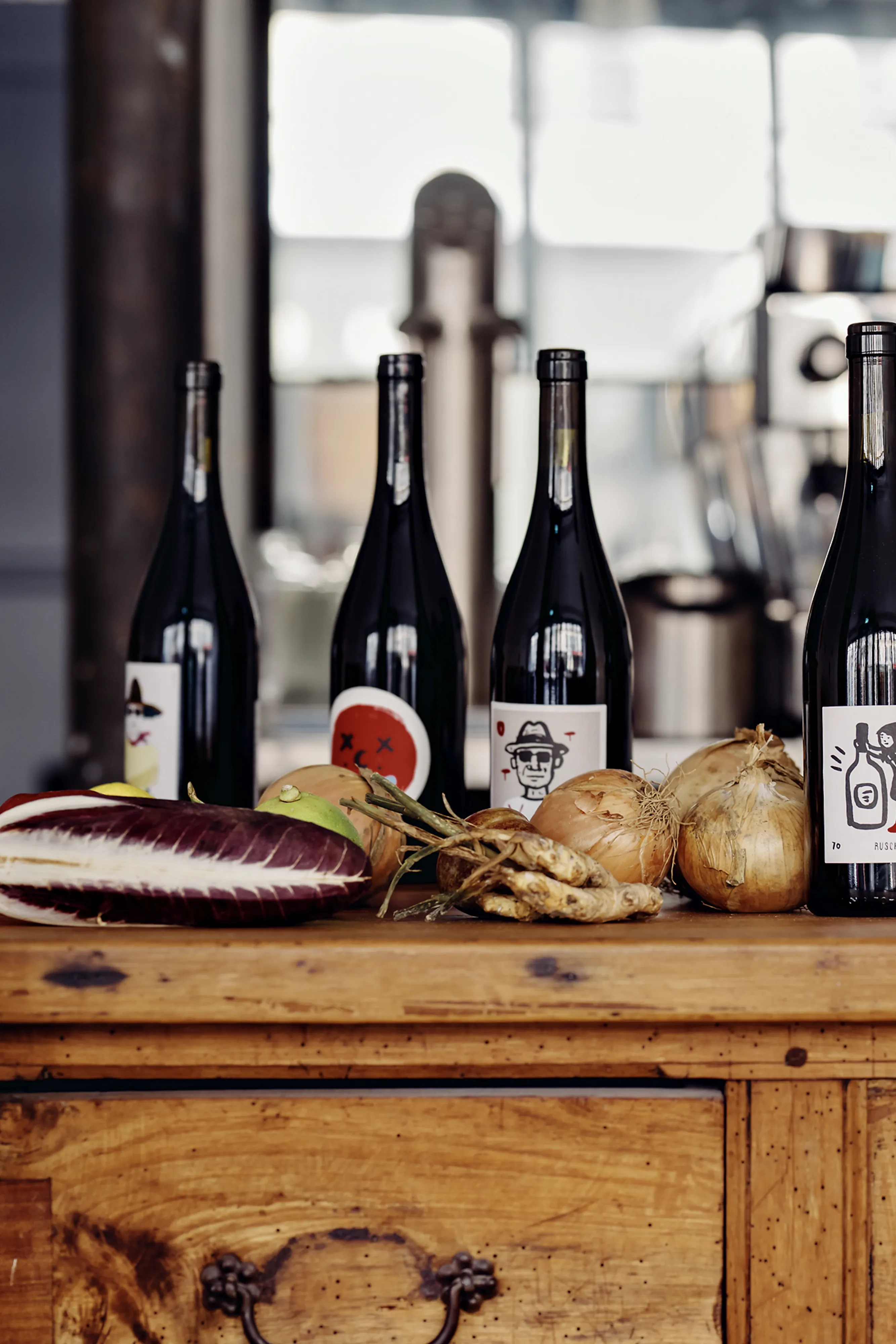 Bouteilles de vin sélectionnées et légumes frais de saison (oignons, radis, citron, gingembre) exposés sur un meuble en bois artisanal, illustrant l’engagement de La Table par Du Pain et Des Idées pour une cuisine locale, authentique et de qualité à Paris.