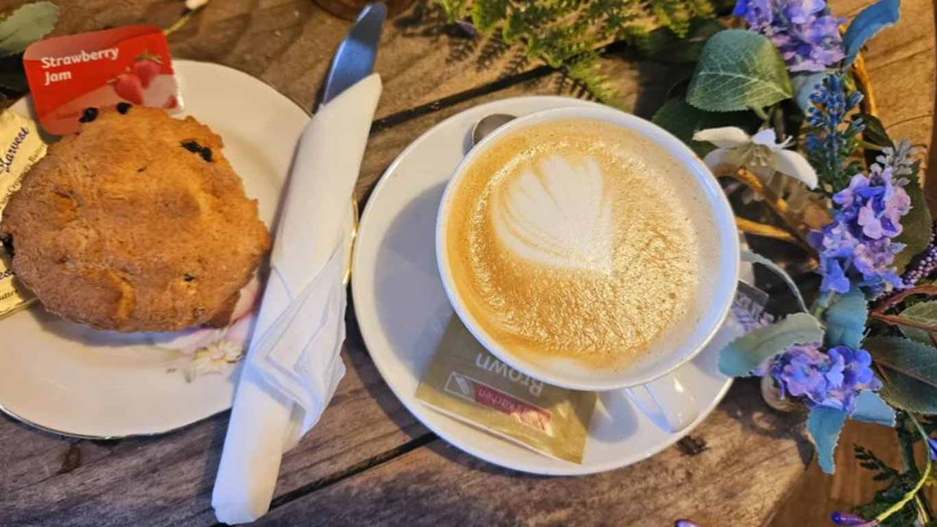 A cup of hot coffee and a freshly baked scone displayed on a table at Roots Café