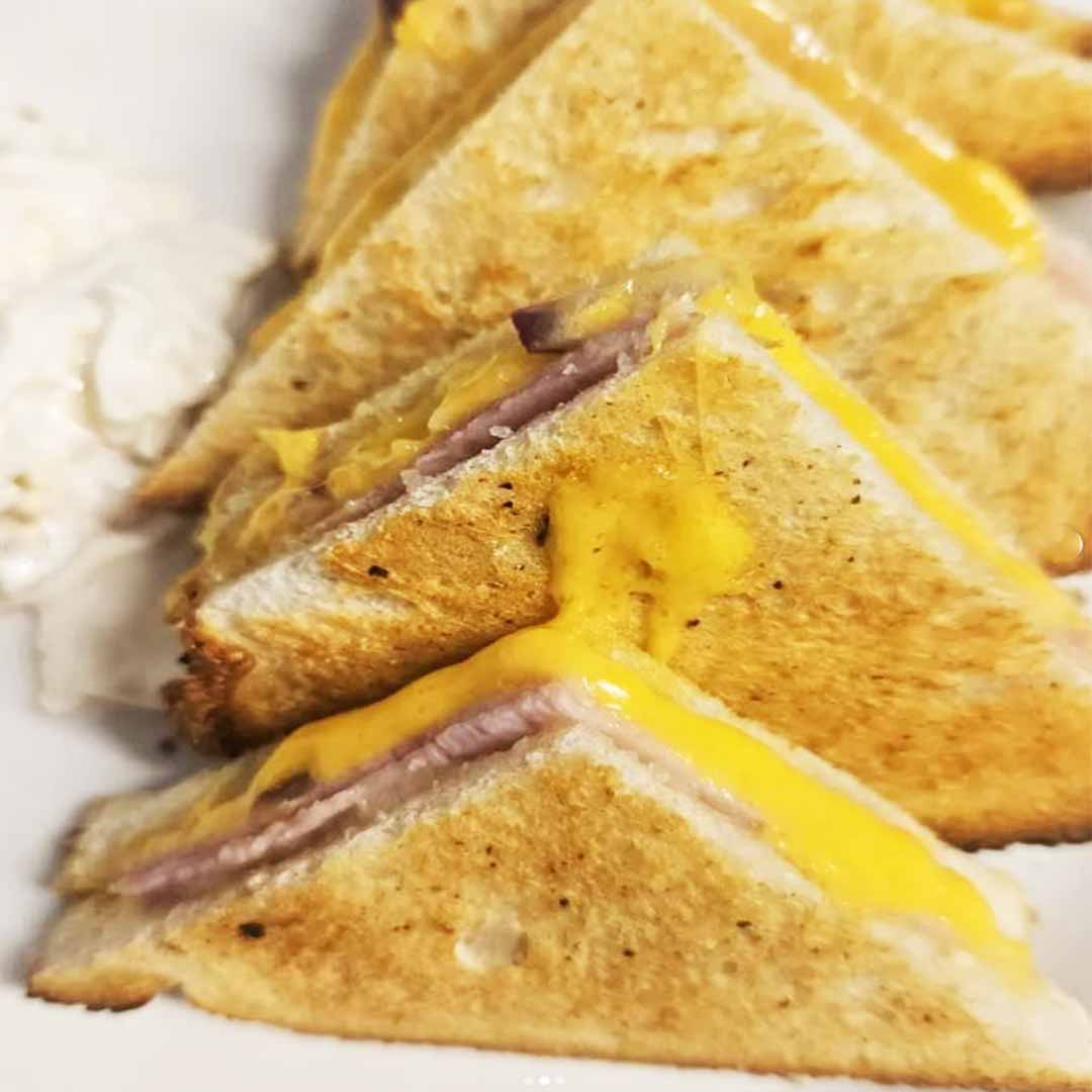 A toasted ham & cheese sandwich cut in quarters and served on a plate at Roots Café