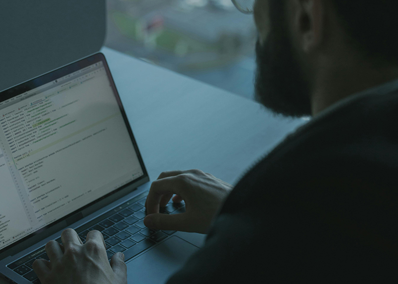Person typing on a laptop with coding text visible on the screen.