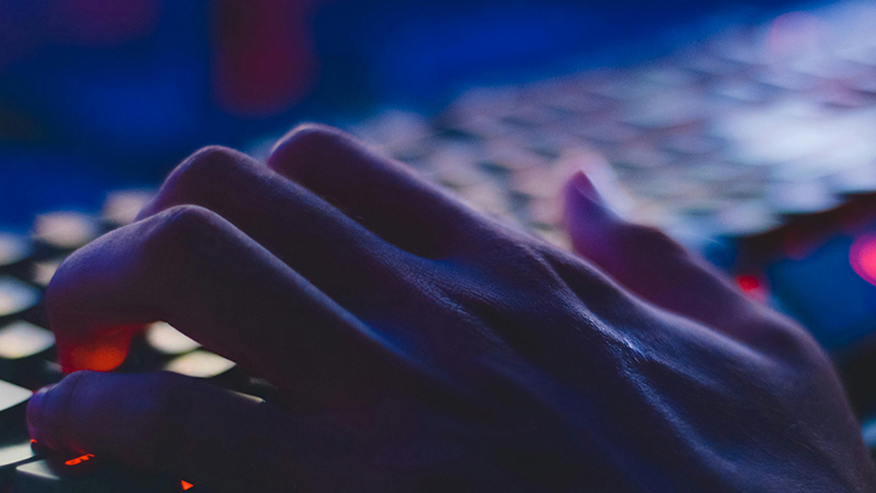 Close-up of a hand typing on a backlit keyboard in low light.