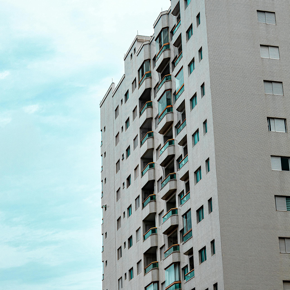 Tall modern apartment building with multiple balconies and windows against a partly cloudy sky.
