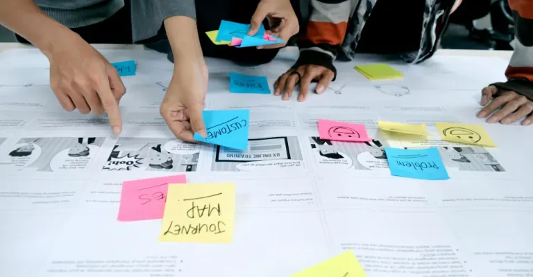 Designers pointing at a customer journey map covered in colorful sticky notes labeled Customer, Problem, and Journey Map during a UX research workshop