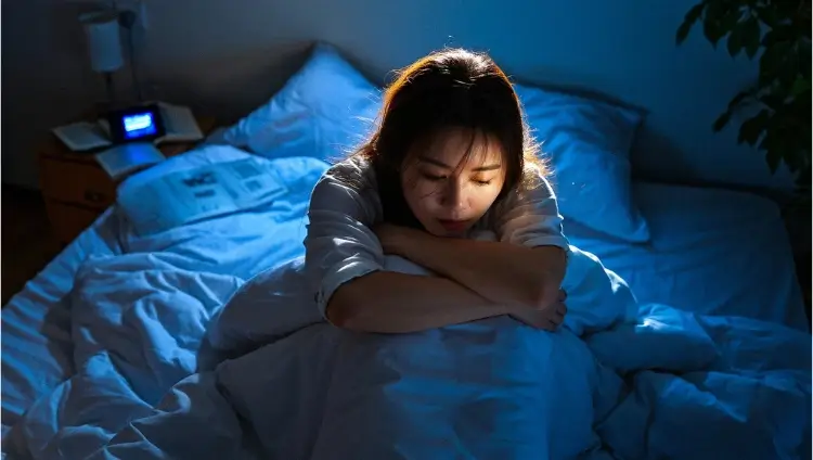 A woman sitting awake in bed at night, struggling with poor sleep quality and insomnia due to neck discomfort.