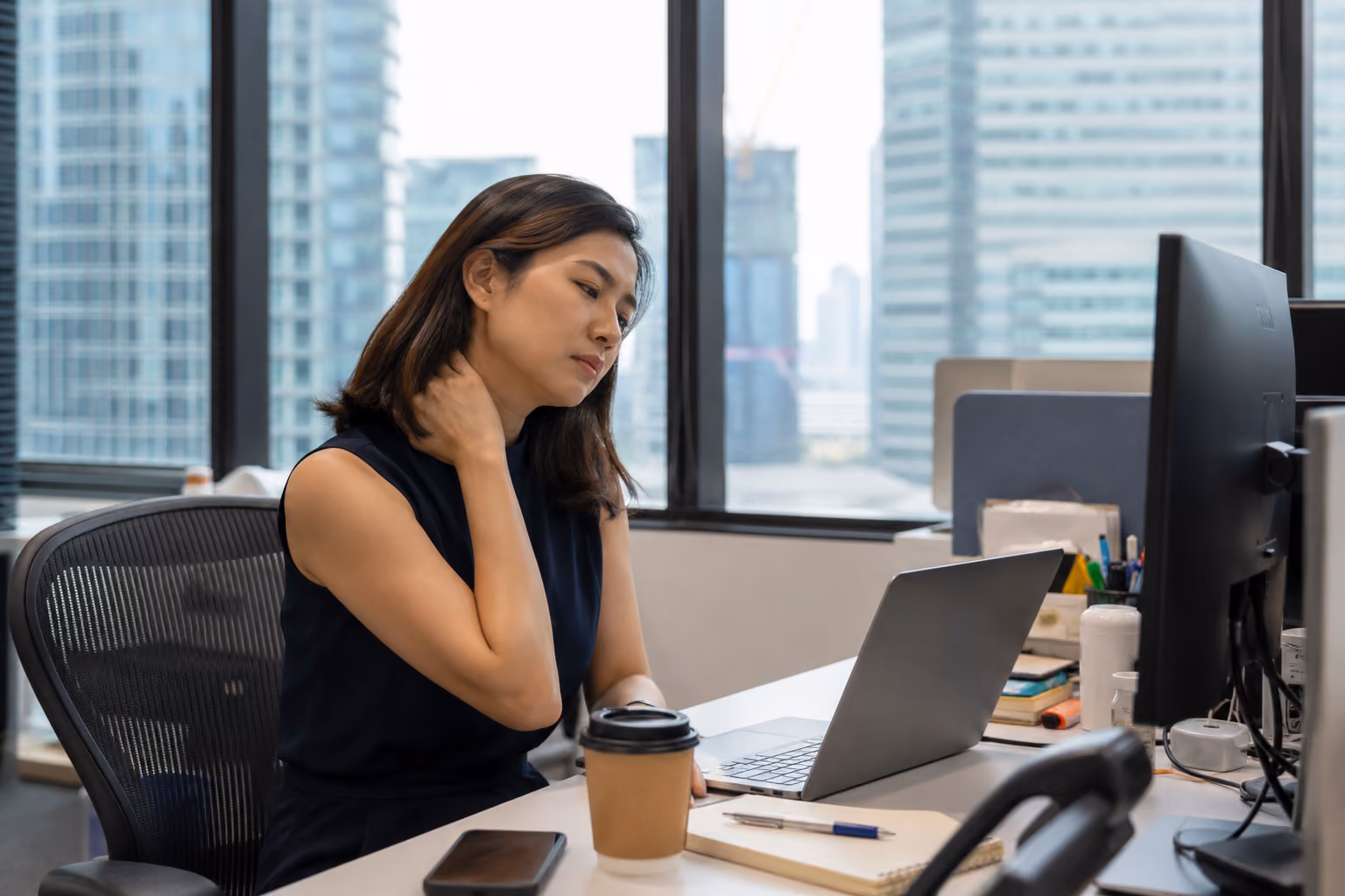 Singapore CBD office worker with chronic neck pain at a desk.