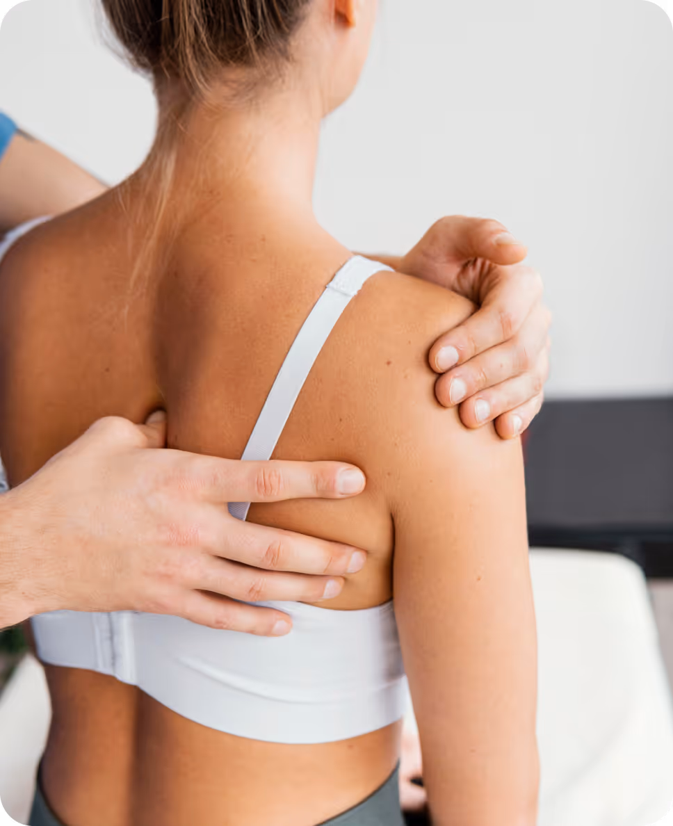 Eine Person trägt ein weißes Sport-BH, während jemand anderes ihre rechte Schulter und den oberen Rücken untersucht oder massiert.