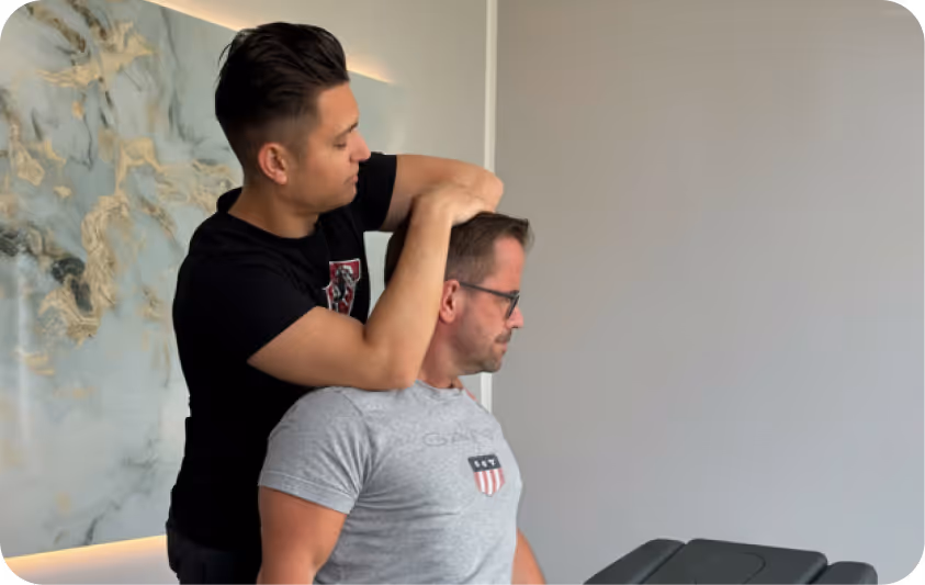 Ein Mann erhält von einem Therapeuten eine Nackenbehandlung in einem hellen Raum mit abstrakter Wandkunst.