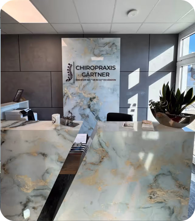 Moderner Empfangsbereich mit Marmor-Theke und Logo der Chiropraxis Gärtner an der Wand.