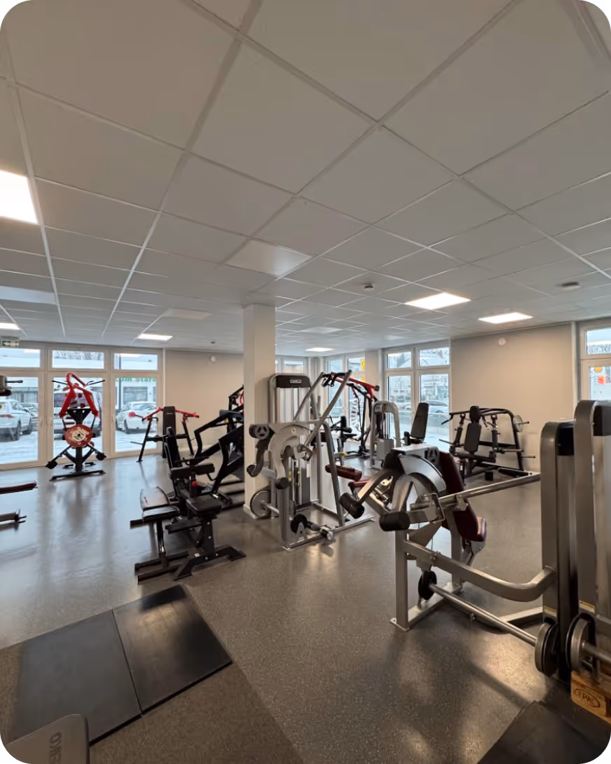 Helle Fitnessstudio bei Chiropraxis, Sven Gärtner mit verschiedenen Krafttrainingsgeräten und großen Fenstern.