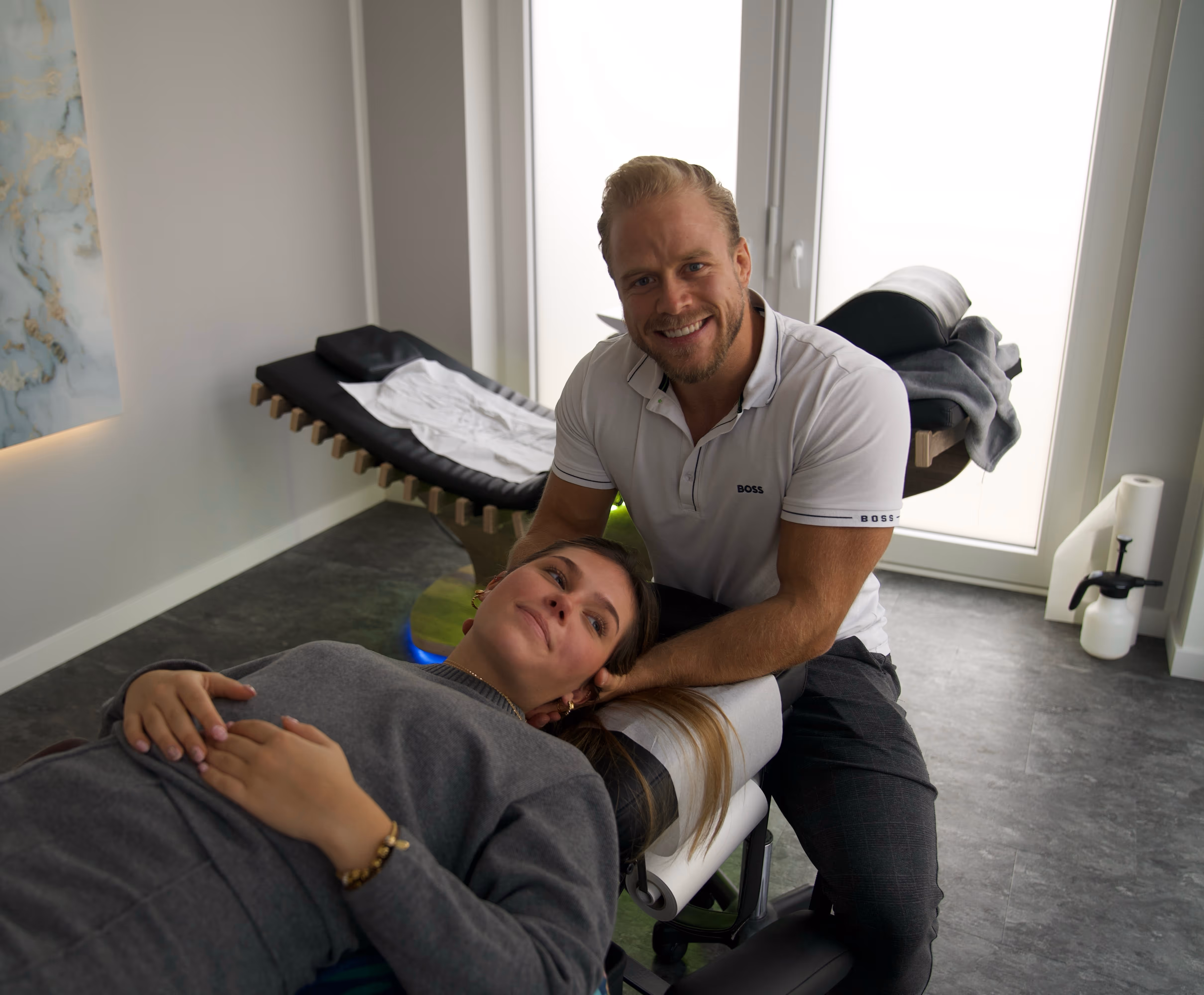 Chiropraktiker in weißem Polo gibt einer Frau eine Nackenbehandlung in einer modernen Praxis.