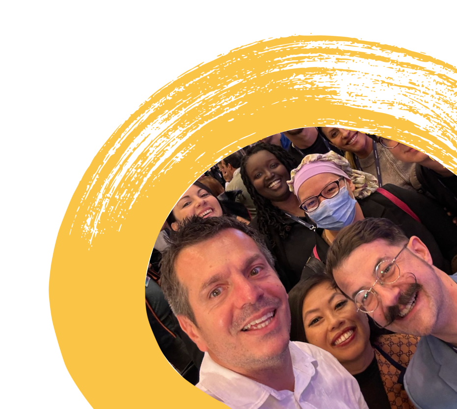 Group selfie of smiling diverse people, including a man with a mustache and glasses, and a woman wearing a face mask and headscarf.