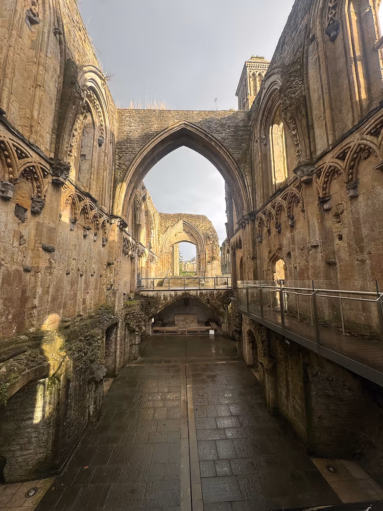 Interior of a historic stone abbey ruin with tall arched windows and a walkway along the right wall.